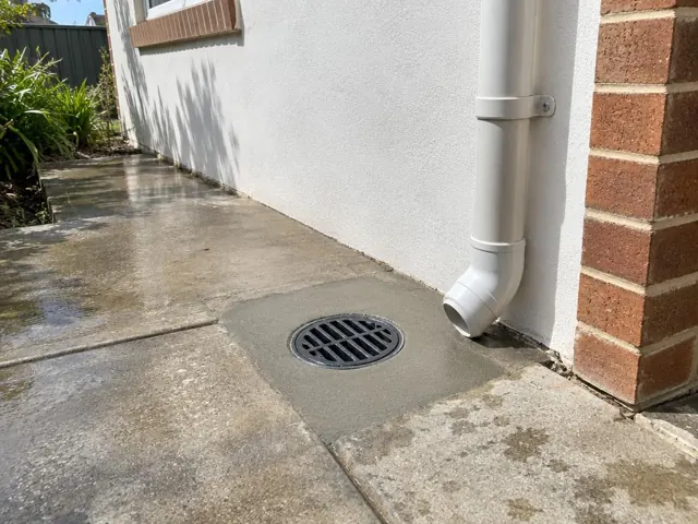 Clean outdoor drain grate beside a concrete path and house wall in Kurri Kurri