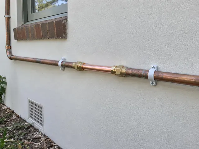 Repaired copper water pipe along an exterior rendered wall beneath a window in Loxford