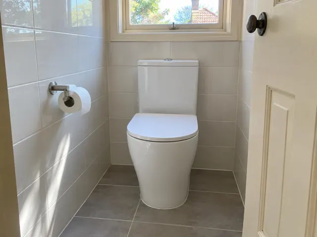 White toilet in a small tiled bathroom with window and wall-hung toilet roll holder in Heddon Greta